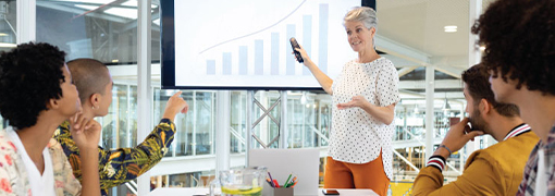 Businesswoman leading a small business workshop, presenting a growth chart to a group at a conference table.