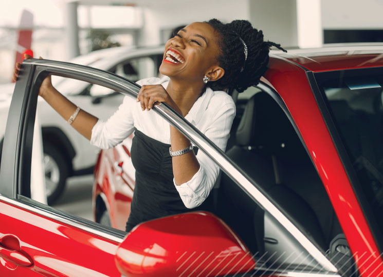 Woman laughs while leaning out of the open driver door of a red car in a dealership showroom.
