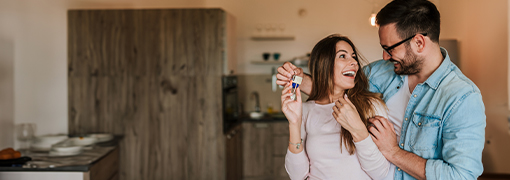 Smiling couple holding house keys together in their new kitchen.