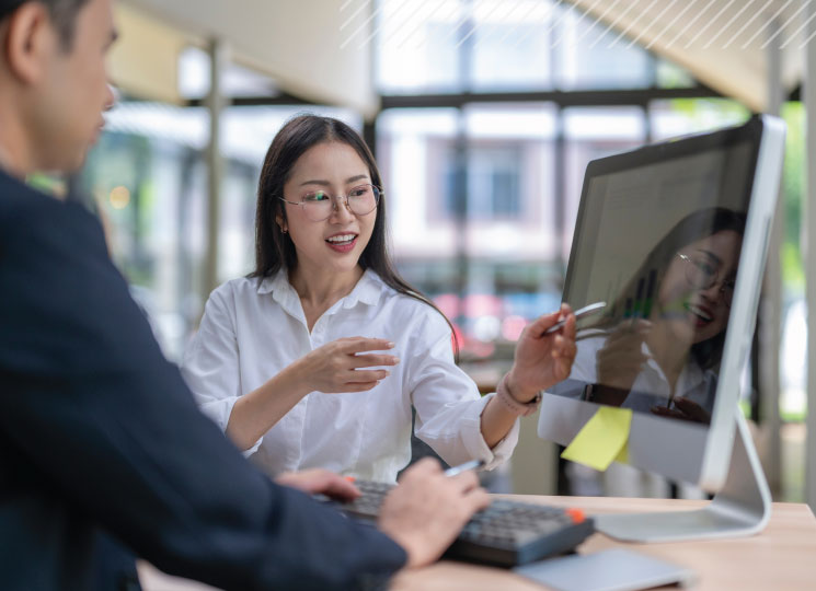 Wealth advisor showing financial data to a client on a desktop computer.