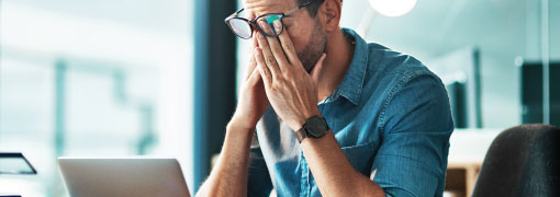Worried man at laptop with hands on his face, overwhelmed by a financial issue.