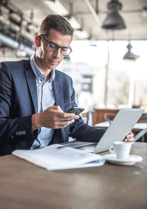 Business owner in Eastern Iowa managing finances on a laptop and phone in a modern café.