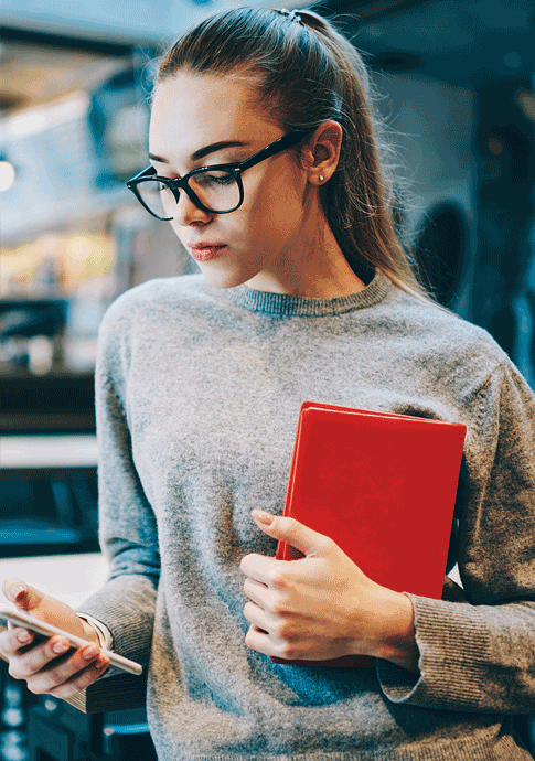 Young woman holding a red notebook and checking her smartphone in a modern workspace.