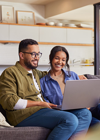 A couple sitting on the couch, looking at a laptop and discussing mortgage options.