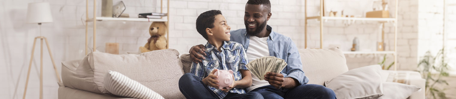 Father and son site on a couch with a piggy bank and money