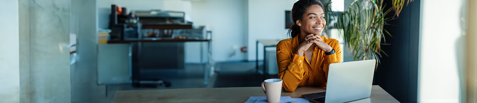 Woman sitting in an office with coffee and her laptop